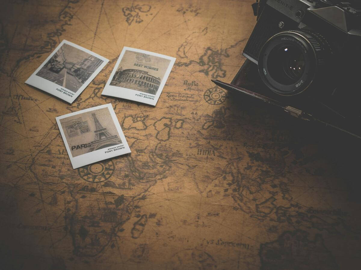 Vintage world map with travel photos and camera representing planning a two week Europe trip itinerary.