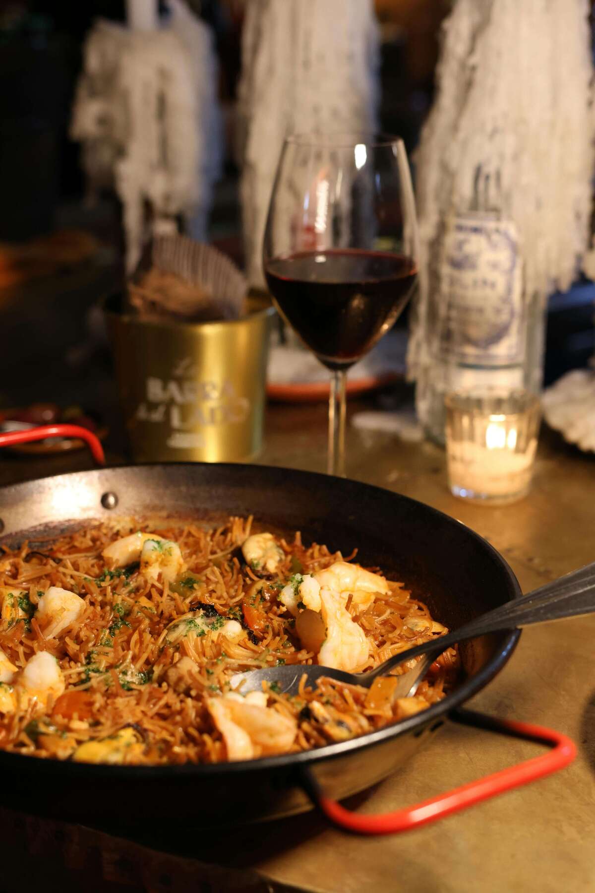 Seafood paella in pan with glass of red wine on table
