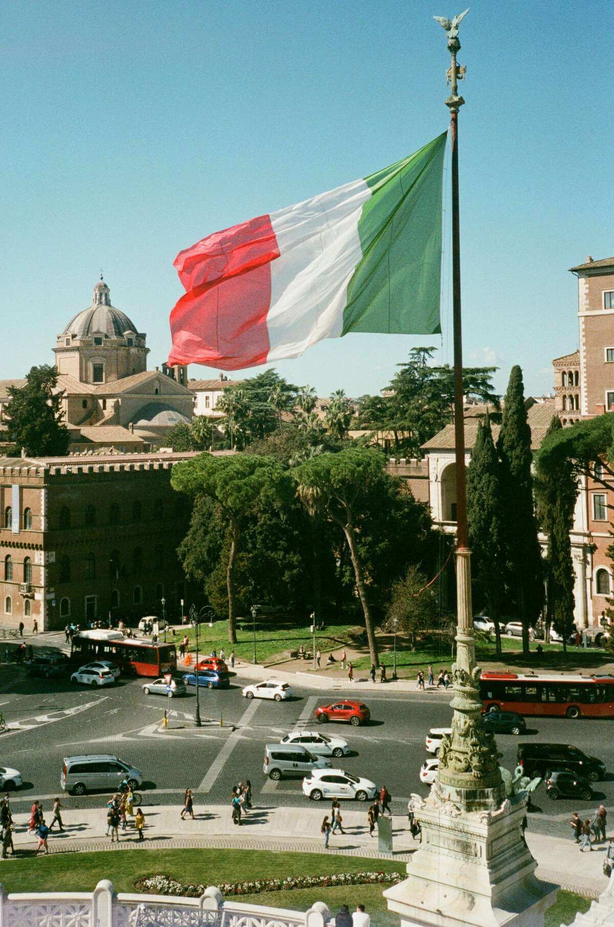 10 Day italy itinerary Italian flag overlooking the historic skyline of Rome during a sunny afternoon.